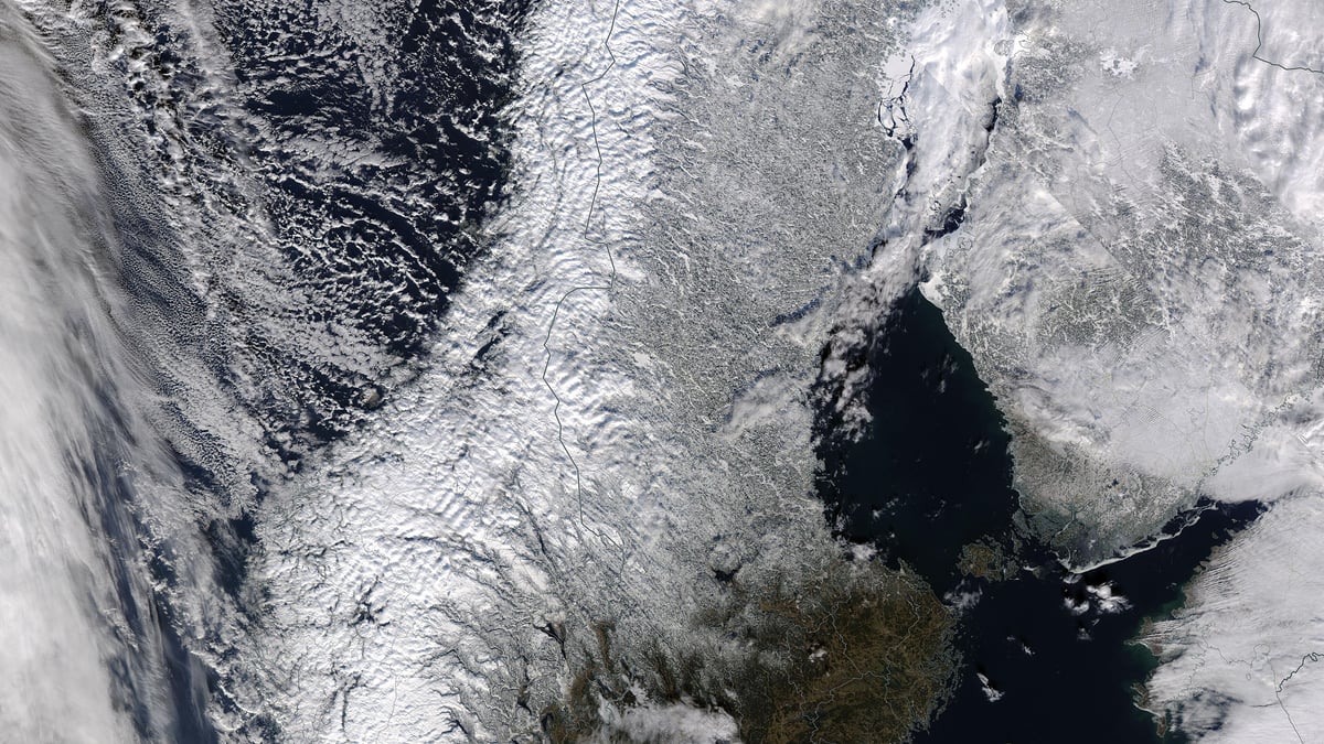 Satellitbild av Skandinavien en vinterdag med snötäckt land och molnsystem över Norska havet och Östersjön.