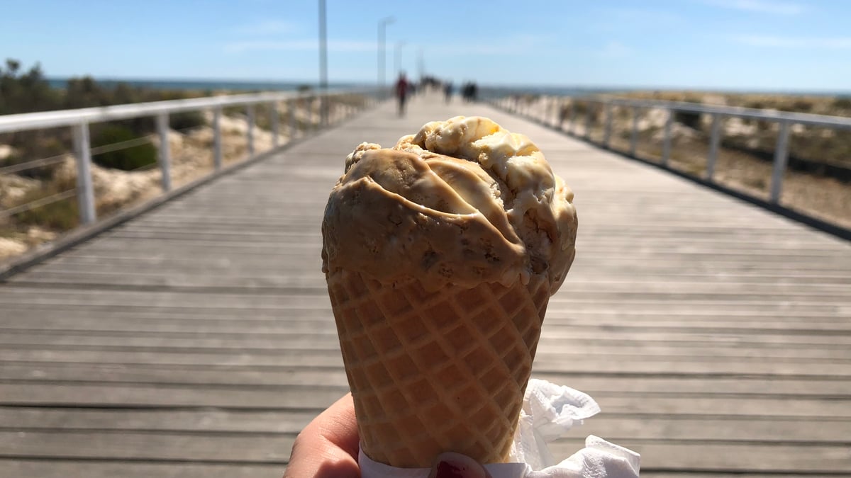 En glasstrut hålls upp på en strandpromenad en solig dag.