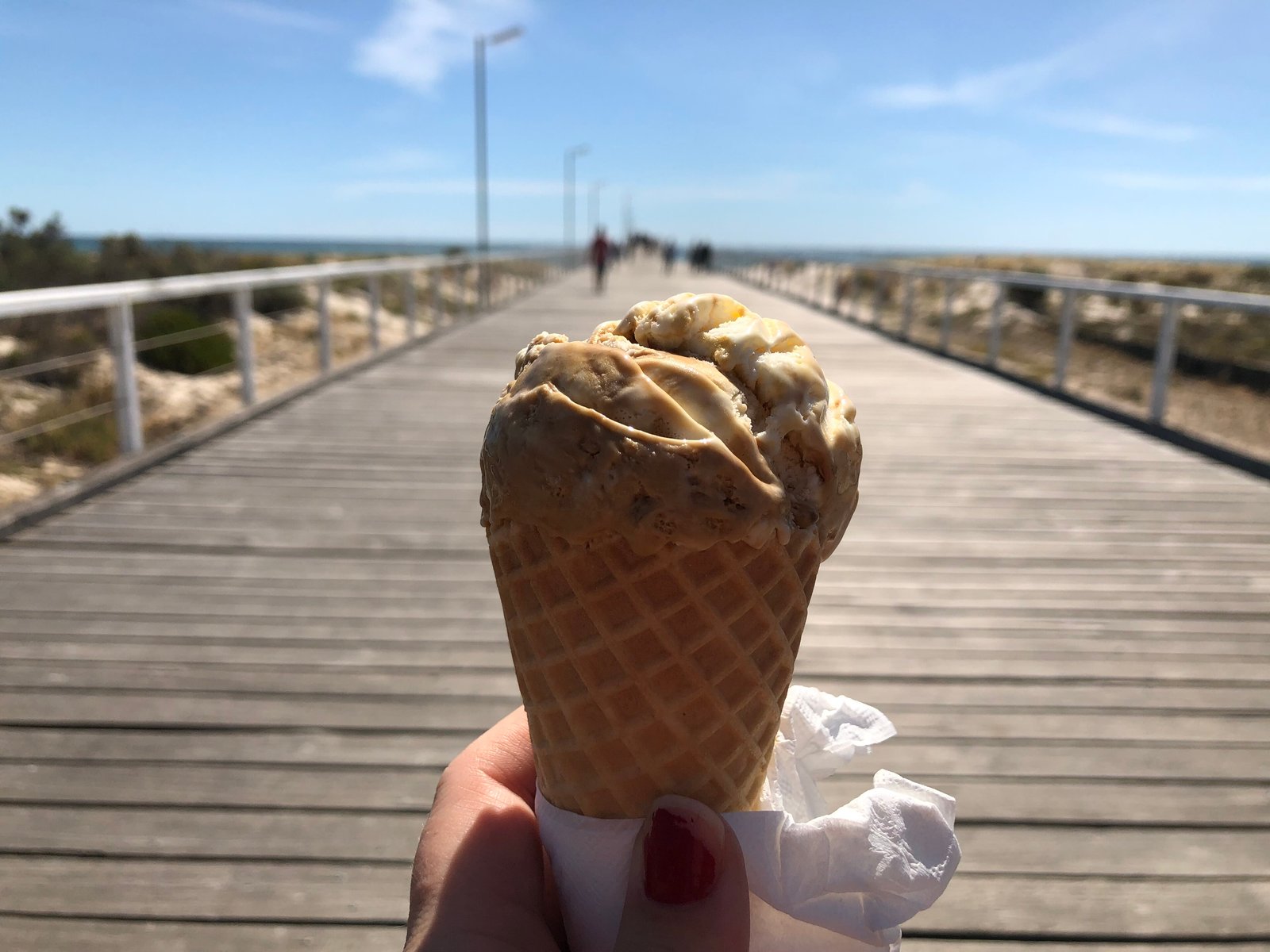 En glasstrut hålls upp på en strandpromenad en solig dag.