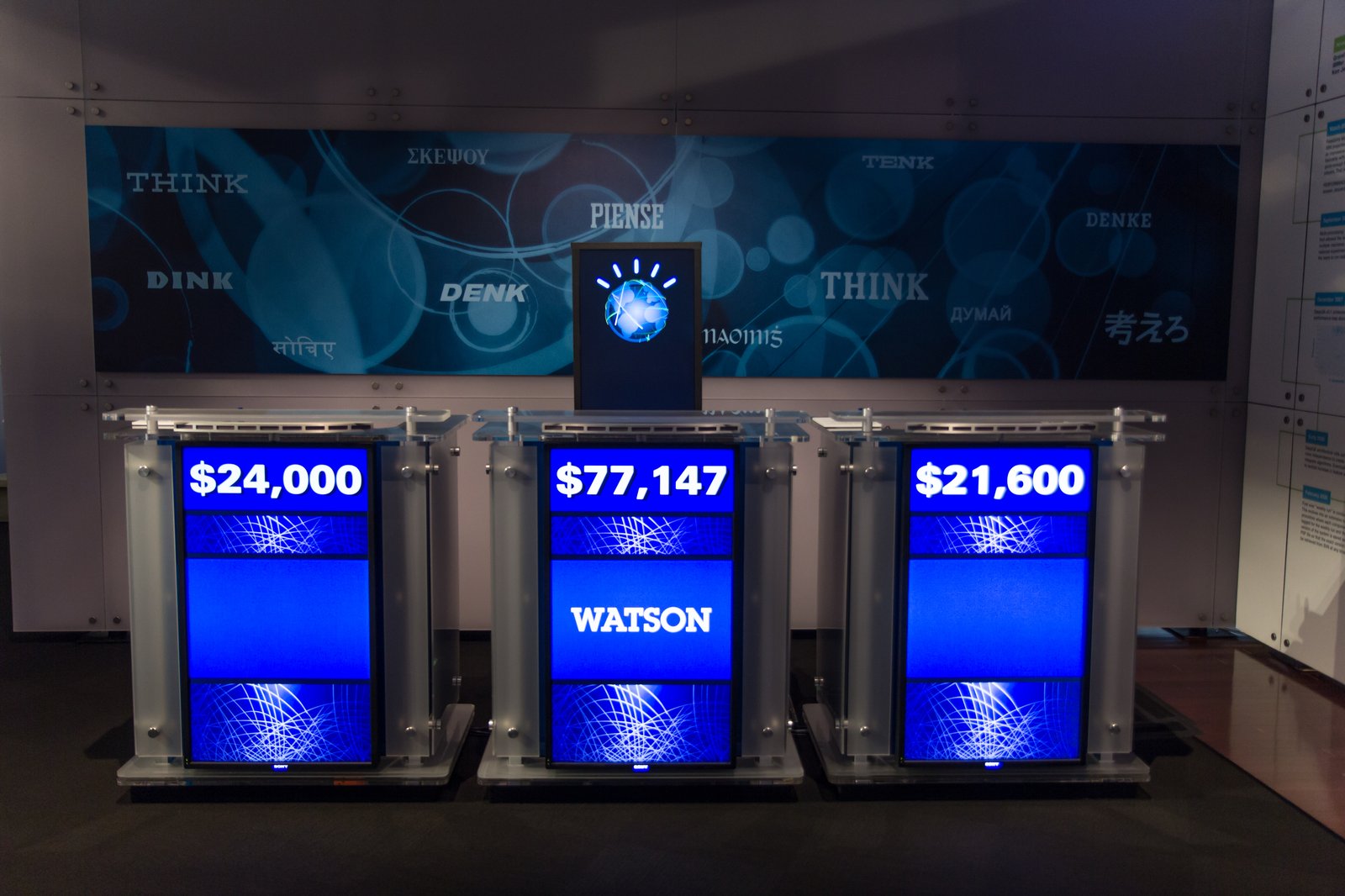 En återskapad Jeopardy-scen med IBM Watsons skärm mellan två andra deltagarplatser.
